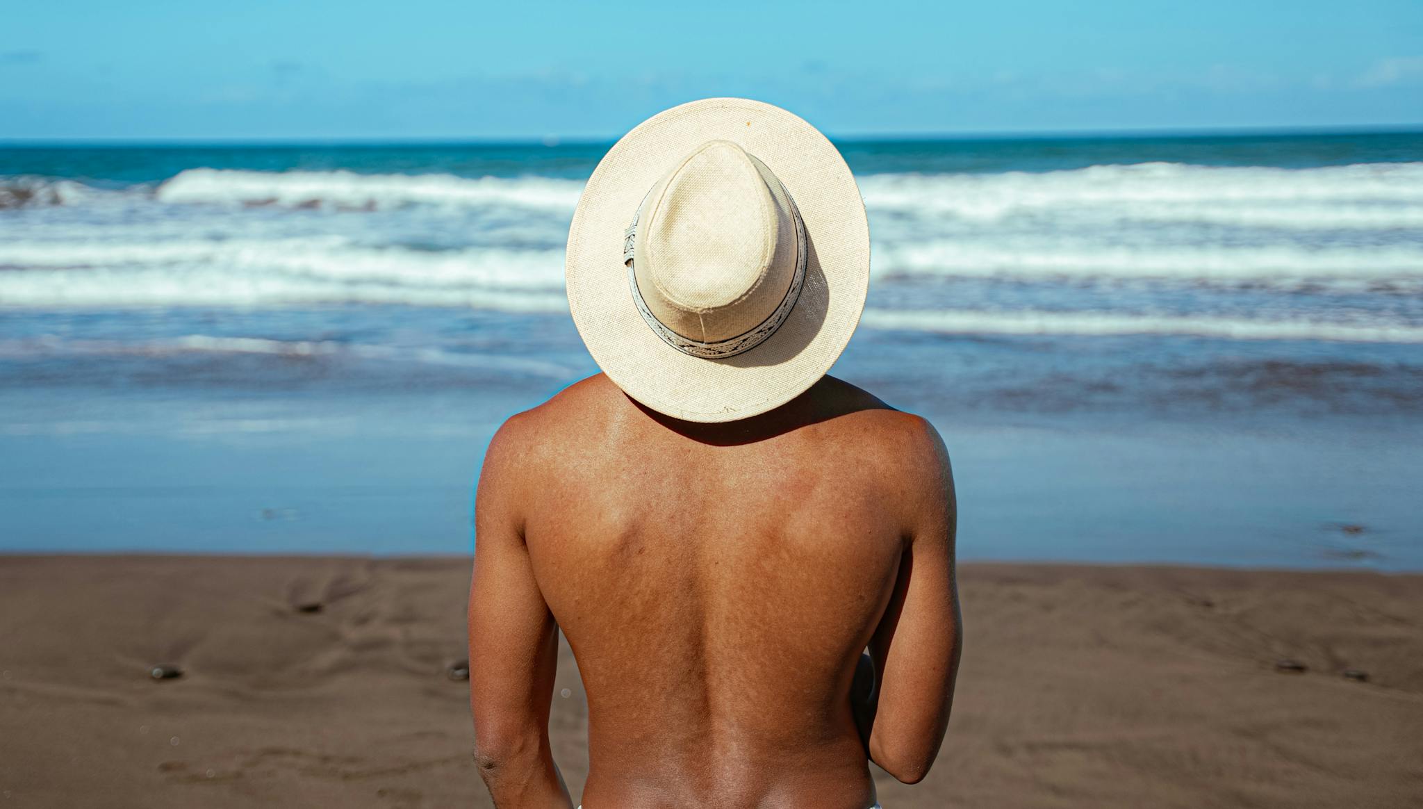 A man wearing a white hat enjoys the sunny weather at a sandy beach on the Canary Islands.
